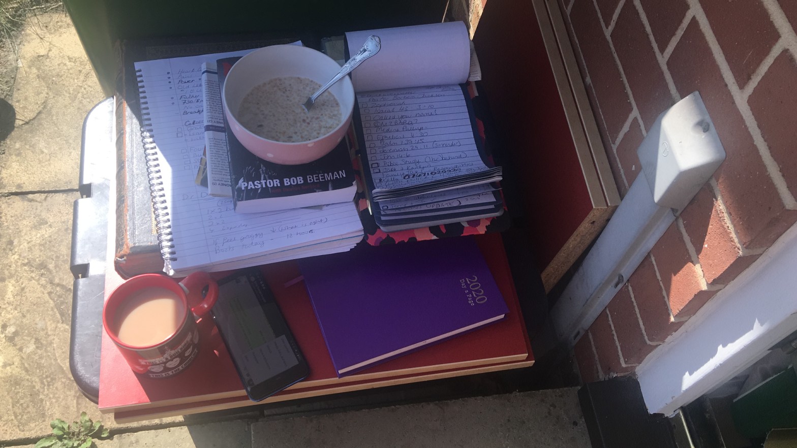 Stack of books, a phone, a diary, a clipboard, a bible, and a bowl of porridge